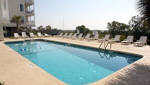 A rectangular swimming pool with clear blue water, surrounded by a concrete deck. There are white lounge chairs aligned along the pool's edge.