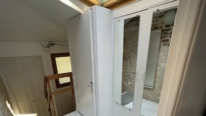Een kamer met witte betegelde vloer, een deur die naar een stenen muur leidt en een dakraam erboven.