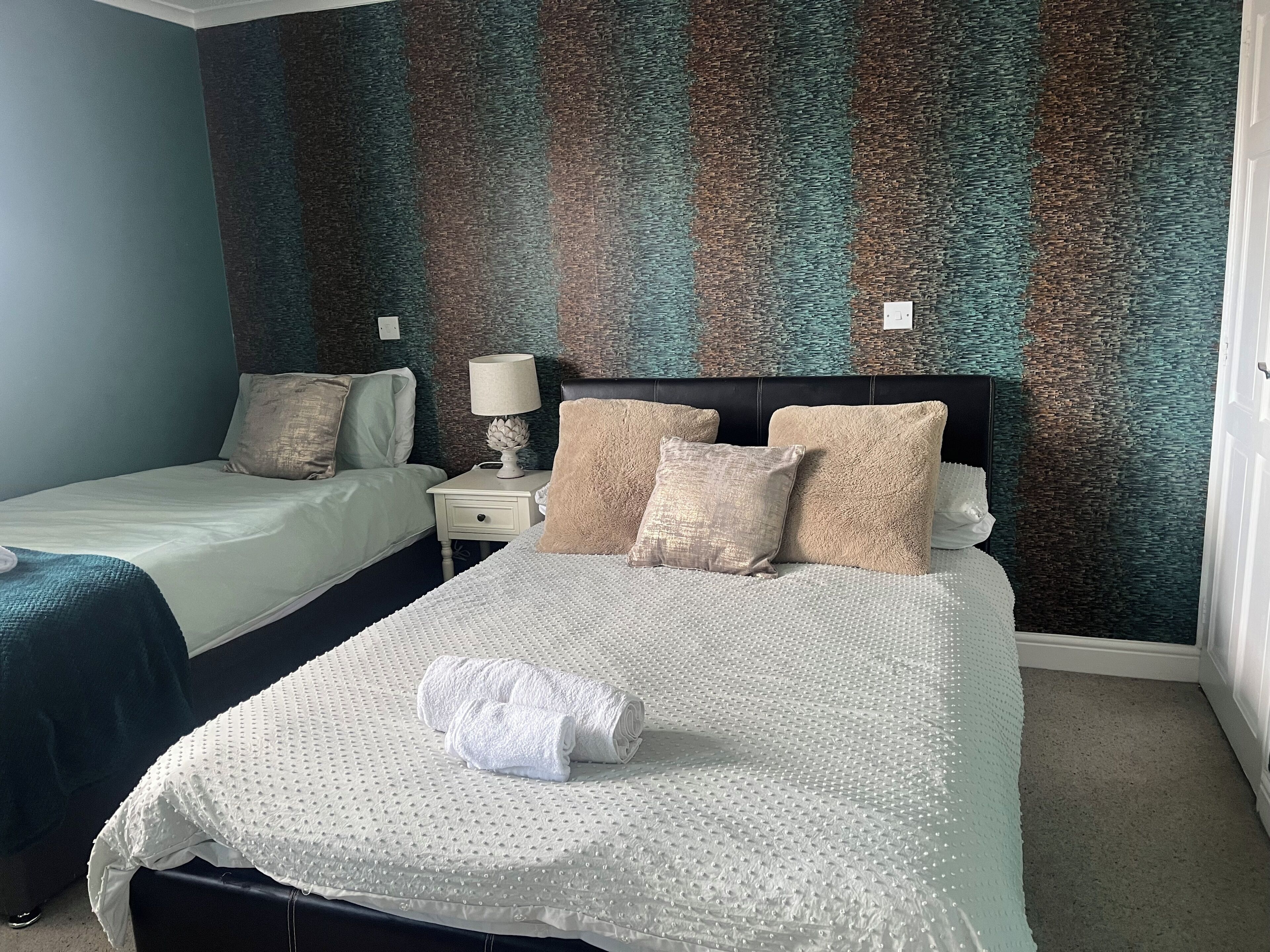 A hotel room with two beds, a nightstand with a lamp, and a textured wall.