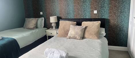 A hotel room with two beds, a nightstand with a lamp, and a textured wall.