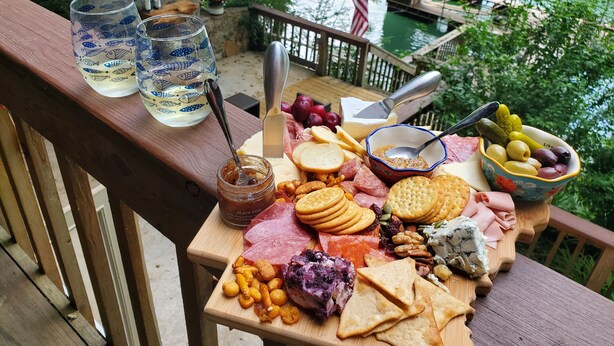 Ein Holztisch mit einer Wurstplatte, Gläsern und Blick auf einen Fluss.