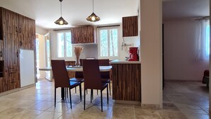 Una cuina moderna amb armaris de fusta, una zona de menjador amb cadires i un gran finestral que ofereix llum natural.
