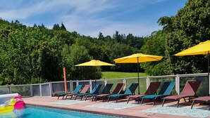 Piscina nítida amb gandules i ombrel·les, envoltada d'un pont de fusta i vistes a arbres.