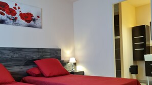Habitació d'hotel amb dos llits, cadascun amb roig i un tabernacle de fusta, i un quadre de flors vermelles a la paret.