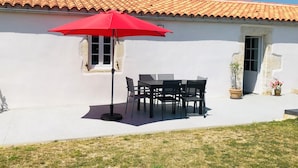 Un bâtiment blanc avec un toit recouvert de tuiles, un parasol rouge et une table entourée de chaises.