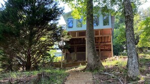 Une maison à deux étages dotée d’une terrasse en bois et d’un chemin en briques menant à l’entrée.