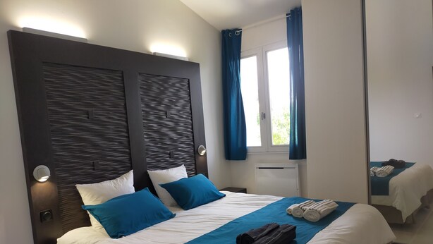 A modern hotel room with a large bed, two bedside lamps, a window with curtains, and a mirror reflecting the room. - T2 R+1 for 2/4 pers, private garden and parking! (Nîmes)