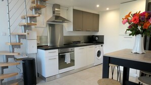 A modern kitchen with a built-in oven, a washing machine, and a dining area with a table and chairs. - T2 R+1 for 2/4 pers, private garden and parking! (Nîmes)