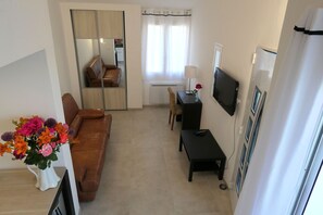 A living room with a brown leather sofa, a small black table, a TV mounted on the wall, and a window with curtains.