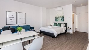 A modern hotel room with a bed, a sofa, a dining table, and a small side table. - Amazing and Perfectly Located Flat by Denstays (Montréal)