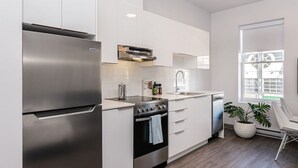 A modern kitchen with stainless steel appliances, white cabinetry, and a window providing natural light. - Amazing and Perfectly Located Flat by Denstays (Montréal)