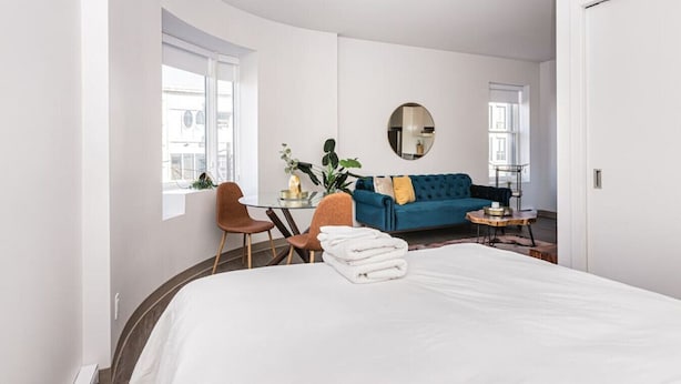 Une chambre d’hôtel moderne avec un grand lit, un canapé bleu, un miroir rond et un coin repas comprenant une table et des chaises.