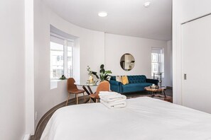 Une chambre d’hôtel moderne avec un grand lit, un canapé bleu, un miroir rond et un coin repas comprenant une table et des chaises.