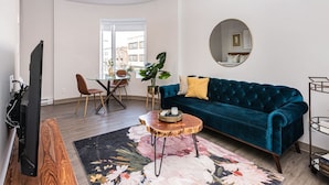 Un salon avec un canapé bleu, une table basse, un téléviseur et un coin repas comprenant des chaises et une table.