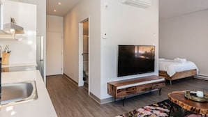 Une chambre d’hôtel moderne dotée d’un téléviseur à écran plat fixé au mur, d’une console en bois, d’un lit avec une literie blanche et d’une petite table ronde sur laquelle se trouve un plateau.