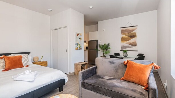 Een moderne hotelkamer met een bed, een grijze bank en een eethoek op de achtergrond.