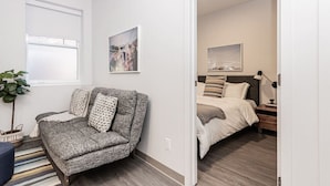 Un dormitorio moderno con un sofá gris, una cama con almohada a rayas, una mesita de noche y un cuadro colgado en la pared.