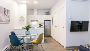 Una cocina moderna con armarios blancos, electrodomésticos de acero inoxidable y una zona de comedor con una mesa de vidrio y sillas coloridas.