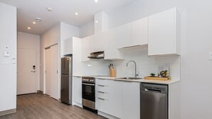 A modern kitchen with white cabinets, stainless steel appliances, and a wooden floor. - Brand New and Perfectly Located Flat in Le Plateau by Denstays (Montréal)