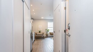 A narrow hallway with a wooden floor, white walls, and a door on the right. There is a bench with a plant and a framed picture on the wall. - Brand New and Perfectly Located Flat in Le Plateau by Denstays (Montréal)