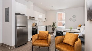 A modern kitchen with stainless steel appliances, a dining area with two chairs, and a large window providing natural light. - St-Denis 209 · Amazing New Apartment Close to Mount Royal (Le Plateau) by Denstays (Montréal)