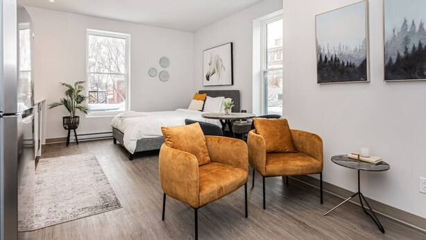A modern bedroom with a bed, two armchairs, a small table, and a window. - St-Denis 209 · Amazing New Apartment Close to Mount Royal (Le Plateau) by Denstays (Montréal)