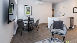 A modern apartment with a dining area, a living room with a sofa, a kitchen, and a large mirror.