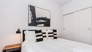 A bedroom with a bed, a nightstand, a lamp, a painting, and a wardrobe.