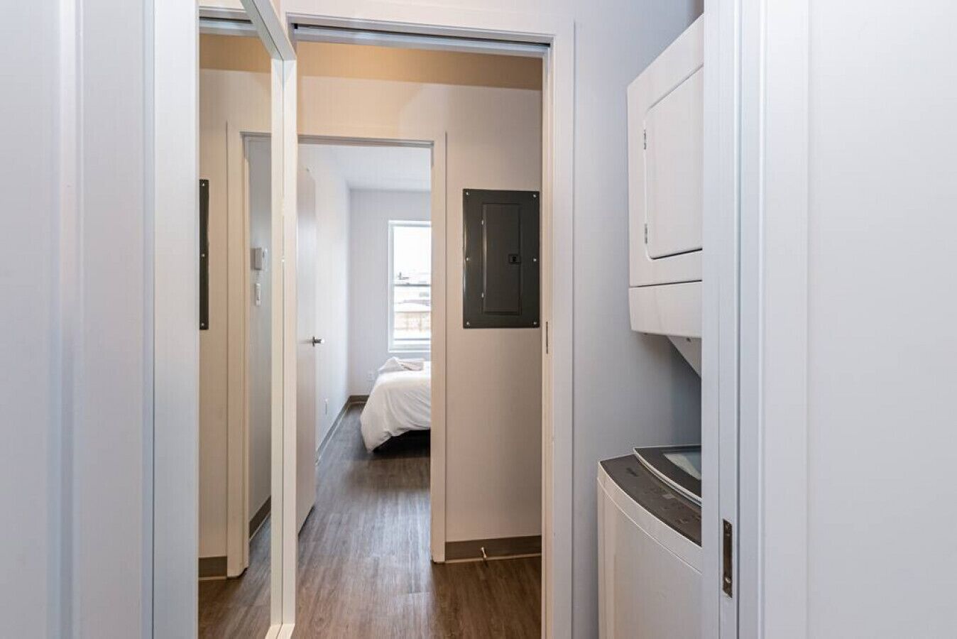 A hallway leading to a bedroom with a bed, a door, and a washing machine.