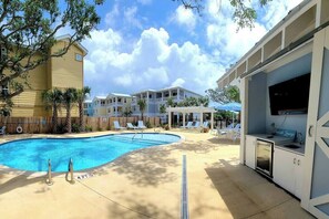A swimming pool with lounge chairs, a bar area, and a poolside view of buildings.