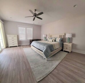 A bedroom with a bed, nightstands, a dresser, a ceiling fan, and a window with blinds.