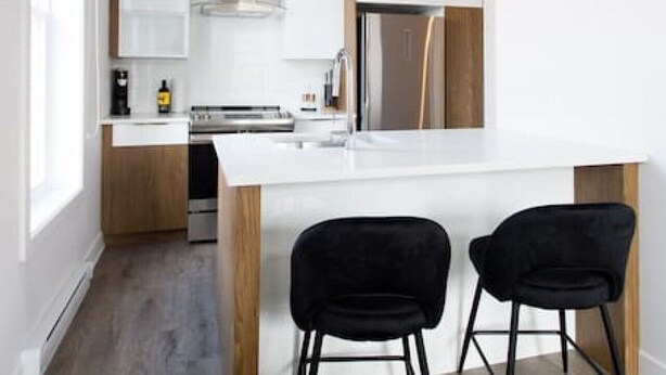 A modern kitchen with a central island, two black chairs, and pendant lights. - Stunning 1 Bedroom in Mile End by Denstays (Montreal)
