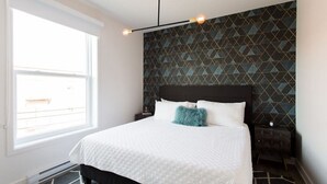 A bedroom with a bed, a window, a geometric patterned wall, and a hanging light fixture. - Stunning 1 Bedroom in Mile End by Denstays (Montreal)