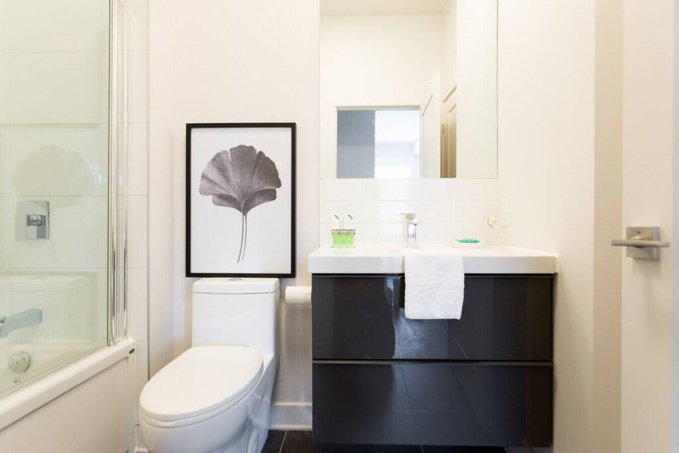 Un baño con inodoro, una obra de arte con una hoja enmarco, lavabo con toalla y espejo.