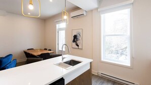 A modern kitchen with a white countertop, a sink, and a dining area with a table and chairs. - Stunning 1 Bedroom in Mile End by Denstays (Montreal)