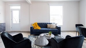 A modern living room with a blue sofa, black chairs, a coffee table, and a large window. - Stunning 1 Bedroom in Mile End by Denstays (Montreal)