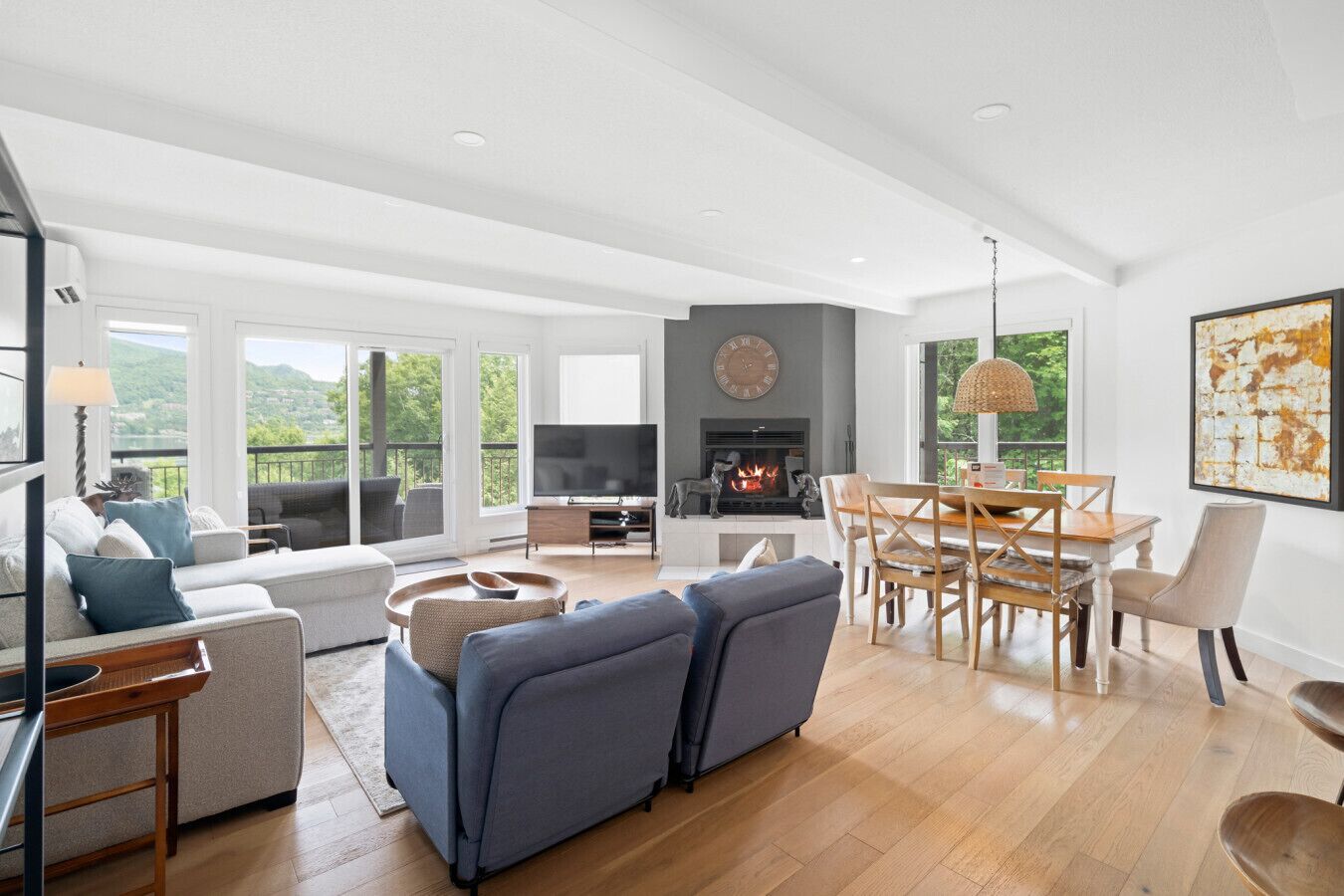 A spacious living room with a fireplace, a dining area, and large windows offering a view of the outdoors.