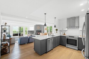 Eine moderne Küche mit grauen Schränken, einer großen Kücheninsel, Edelstahlgeräten und einem Essbereich mit Sofa und Tisch.