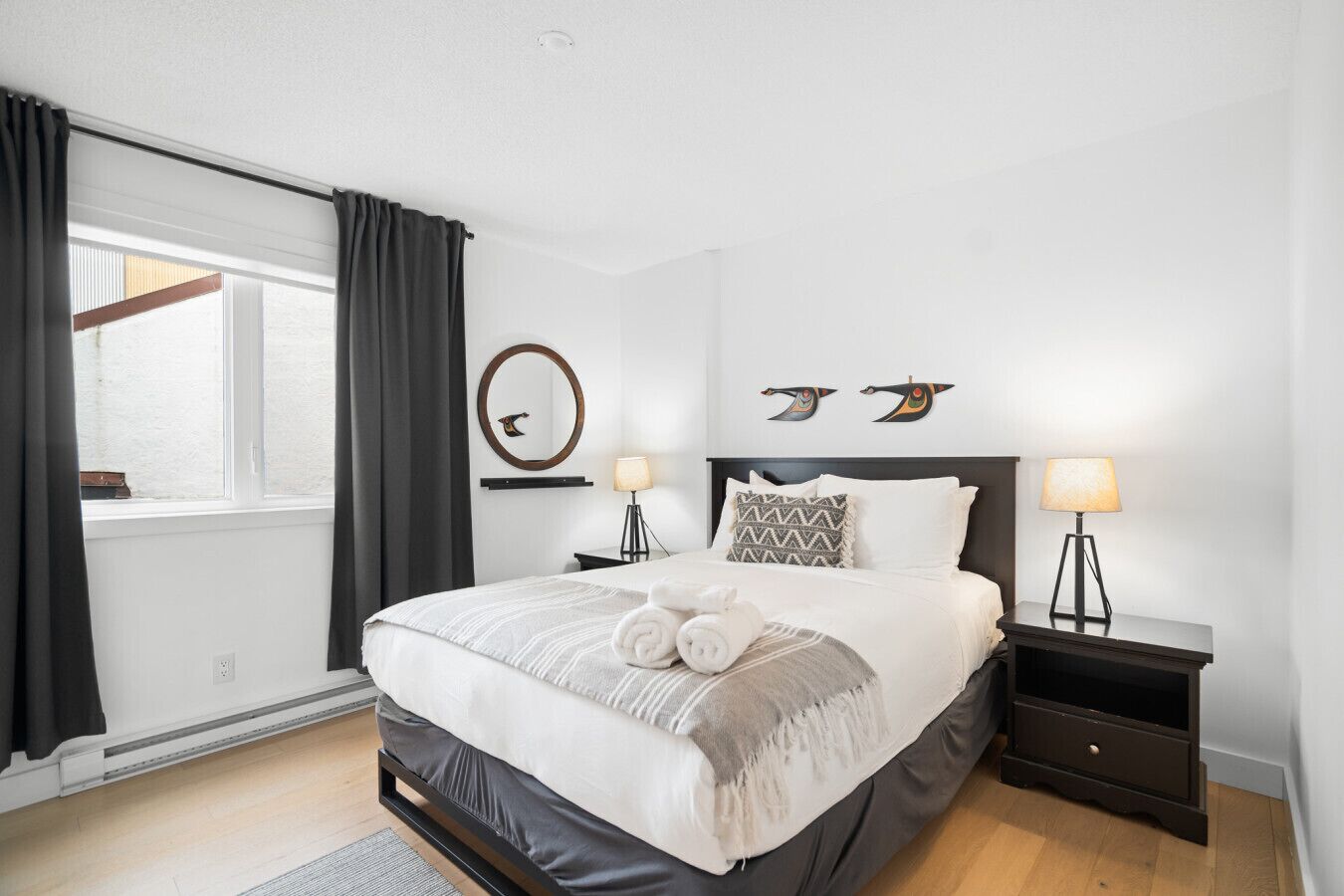 Ein modernes Schlafzimmer mit einem großen Bett, zwei Nachttischlampen, einem runden Spiegel und Wandbildern.