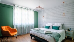 Une chambre à coucher avec un lit, une chaise, une table de chevet et une fenêtre avec des rideaux.