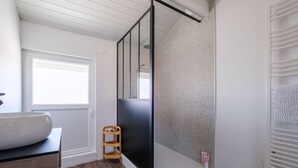 Une salle de bain avec un grand lavabo blanc, une étagère en bois, une cabine de douche en verre et un porte-serviettes blanc.