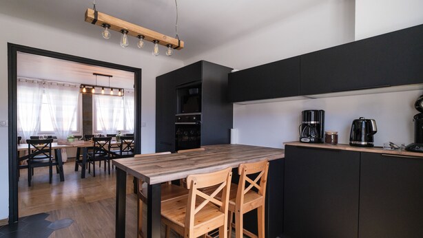 Ett modernt kök med ett matbord och stolar i trä, en inbyggd ugn och en kaffebryggare.