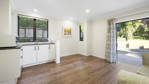 A modern kitchen with white cabinets and a wooden countertop, a dining area with a yellow chair, and a large sliding glass door leading to a garden. - Kapiti Views - Waikanae Beach Holiday Home (Waikanae Beach)