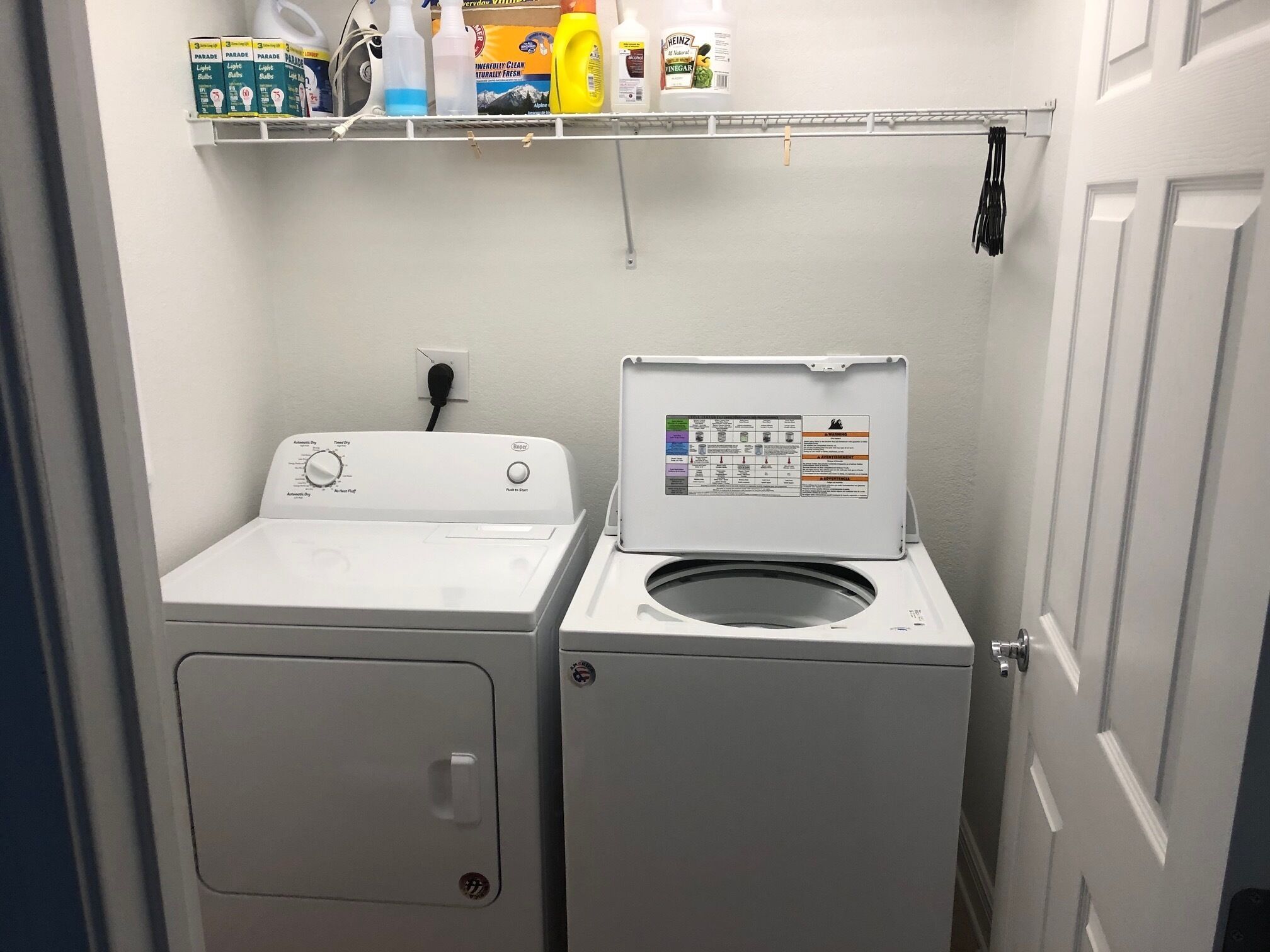 Un espace buanderie comprenant un lave-linge et un sèche-linge à chargement frontal, une étagère au-dessus pour ranger les produits de nettoyage, et une porte sur le côté droit.