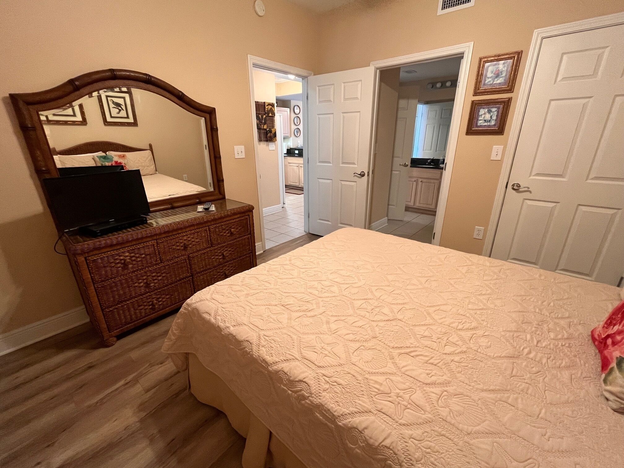 A bedroom with a bed, dresser, and a television on the dresser. There are two doors leading to other rooms.