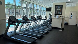 Gimnasio con cintas de correr, bicicletas estáticas y una zona de piscina visibles a través de amplios ventanales.