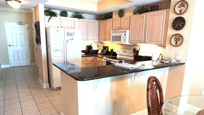 Una cocina con una isla central, armarios de color claro, microondas y refrigerador.