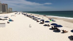 Una playa con filas de sillas y sombrillas, una carpa y un muelle al fondo.