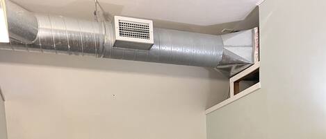 En køjeseng med træramme og gråt sengetøj, en trækommode til højre, og en ventilationsrist over sengen.