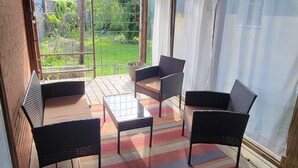 Een overdekt terras met houten vloer, een kleurrijk vloerkleed en rieten meubels.